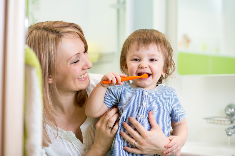 Woman holding child brushing teeth