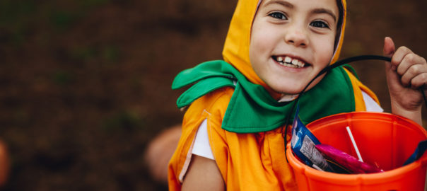 Close up portrait of cute little girl in Halloween costume holding pumpkin bucket outdoors at the park. Little girl child out for trick or treating on Halloween.