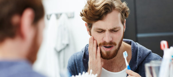 Man with sensitive teeth touching his cheek