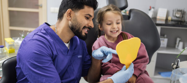 The image shows a pediatric dentist treating a young patient. The image serves to shows the benefits of pediatric dentistry and visually represents what ages pediatric dentists treat.