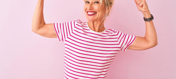 Smiling woman flexing muscles, front angle, striped pink and white shirt against pink background