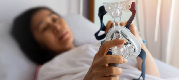 Woman lying in bed in background, holding anesthesia mask in foreground